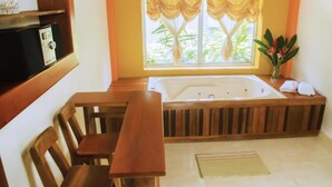 A room with a wooden bench, a large bathtub, and a window with curtains.