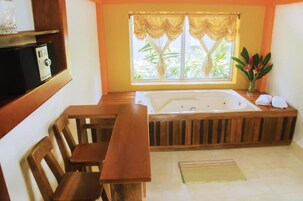 Una habitación con un banco de madera, una bañera grande y una ventana con cortinas.