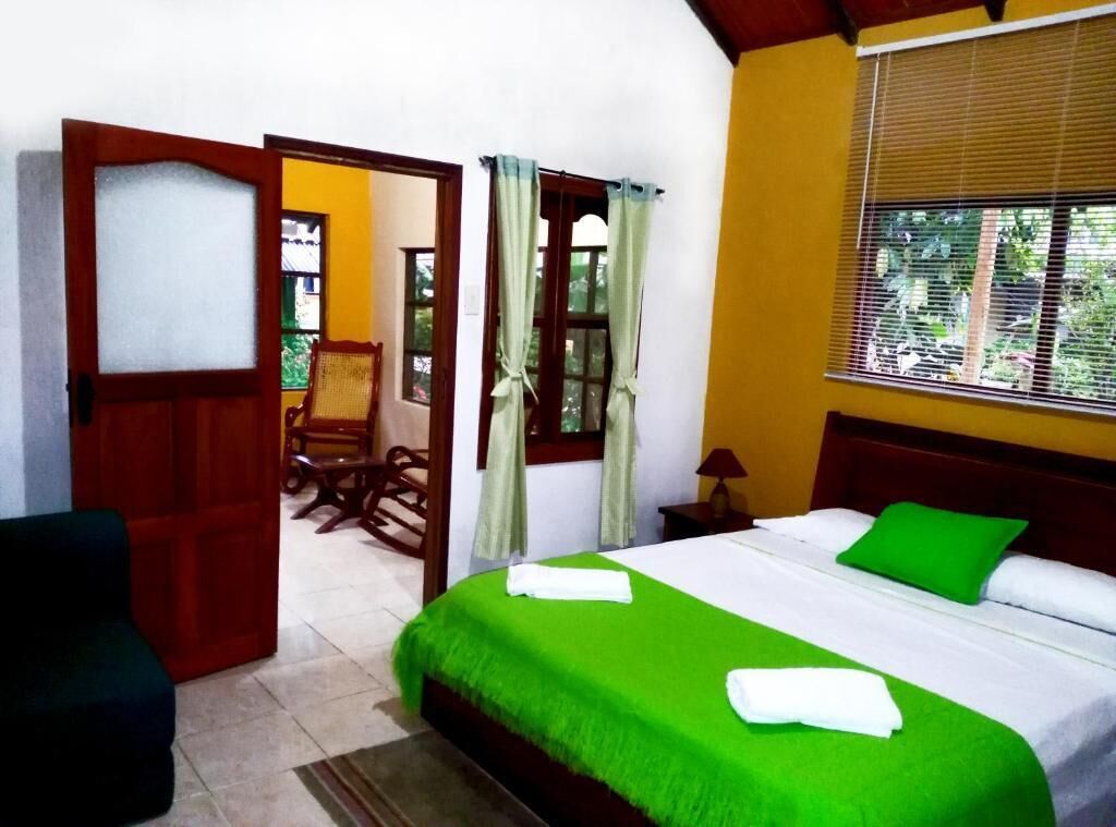 A hotel room with a bed, a chair, a table, and a window with curtains.