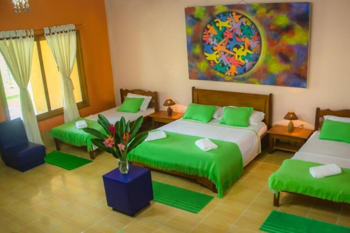 Une chambre d’hôtel avec deux lits simples, un grand tableau accroché au mur et une plante en pot posée sur le sol.