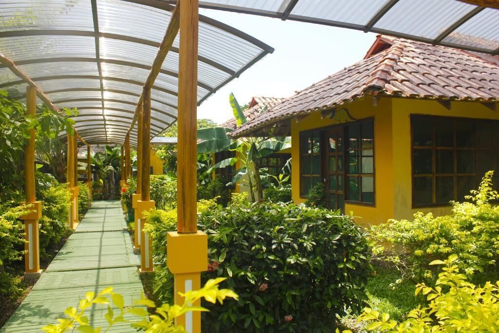 A greenhouse structure with a glass roof, a pathway, and a yellow building with windows.
