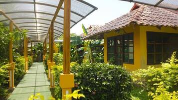 A greenhouse structure with a glass roof, a pathway, and a yellow building with windows.