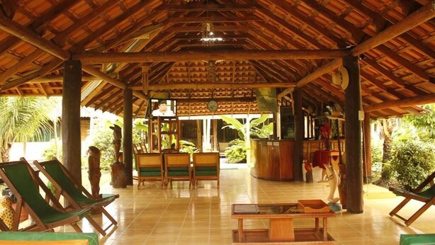 A covered outdoor lounge area with wooden furniture and a tiled floor.