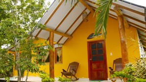 A yellow building with a wooden porch, two rocking chairs, and a red door.