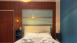 Un lit bien fait, recouvert d’une couvre-lit à motifs, avec deux serviettes pliées, une table de chevet avec une lampe et une armoire en bois.