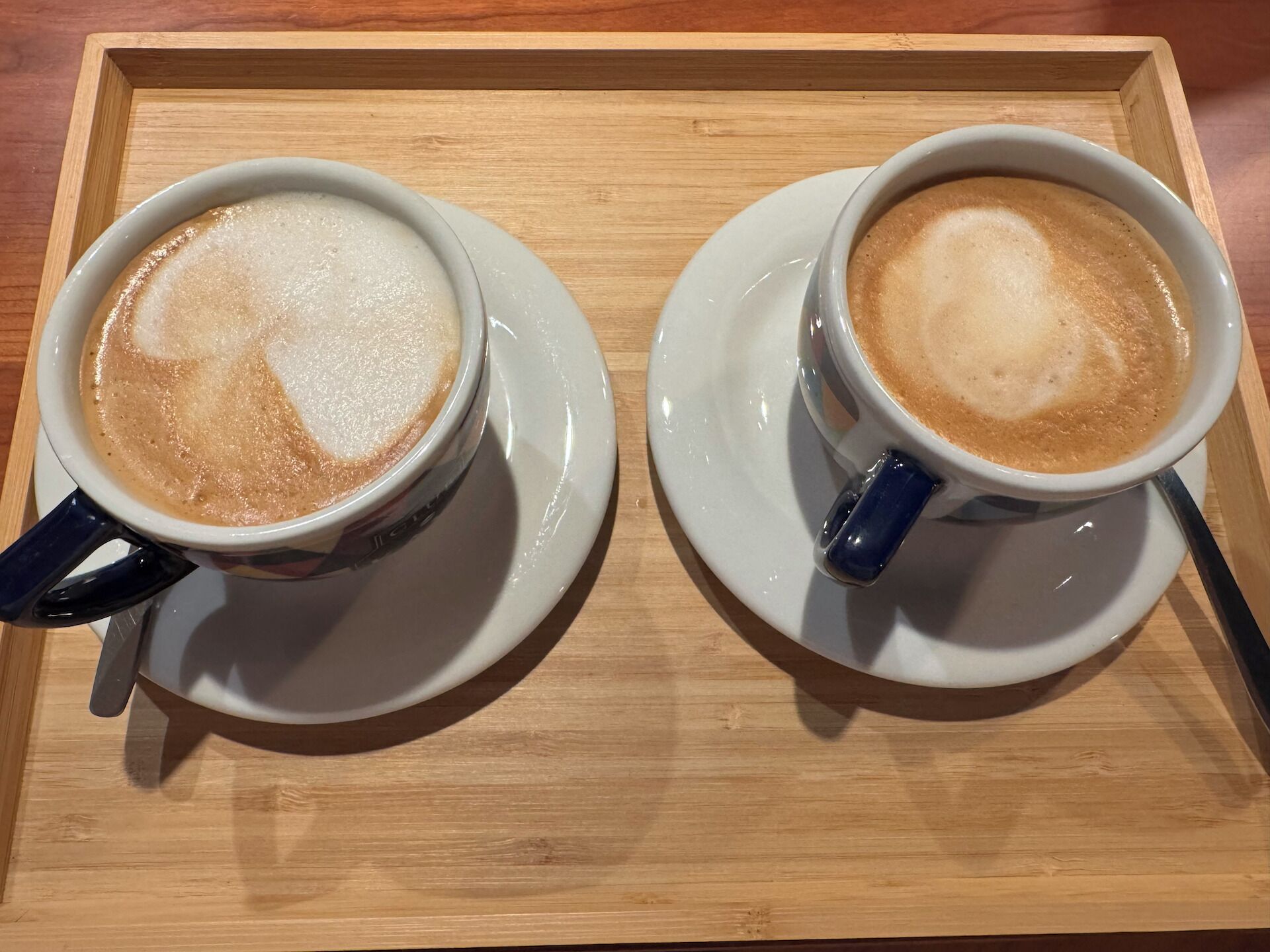 Two cups of coffee on a wooden tray.