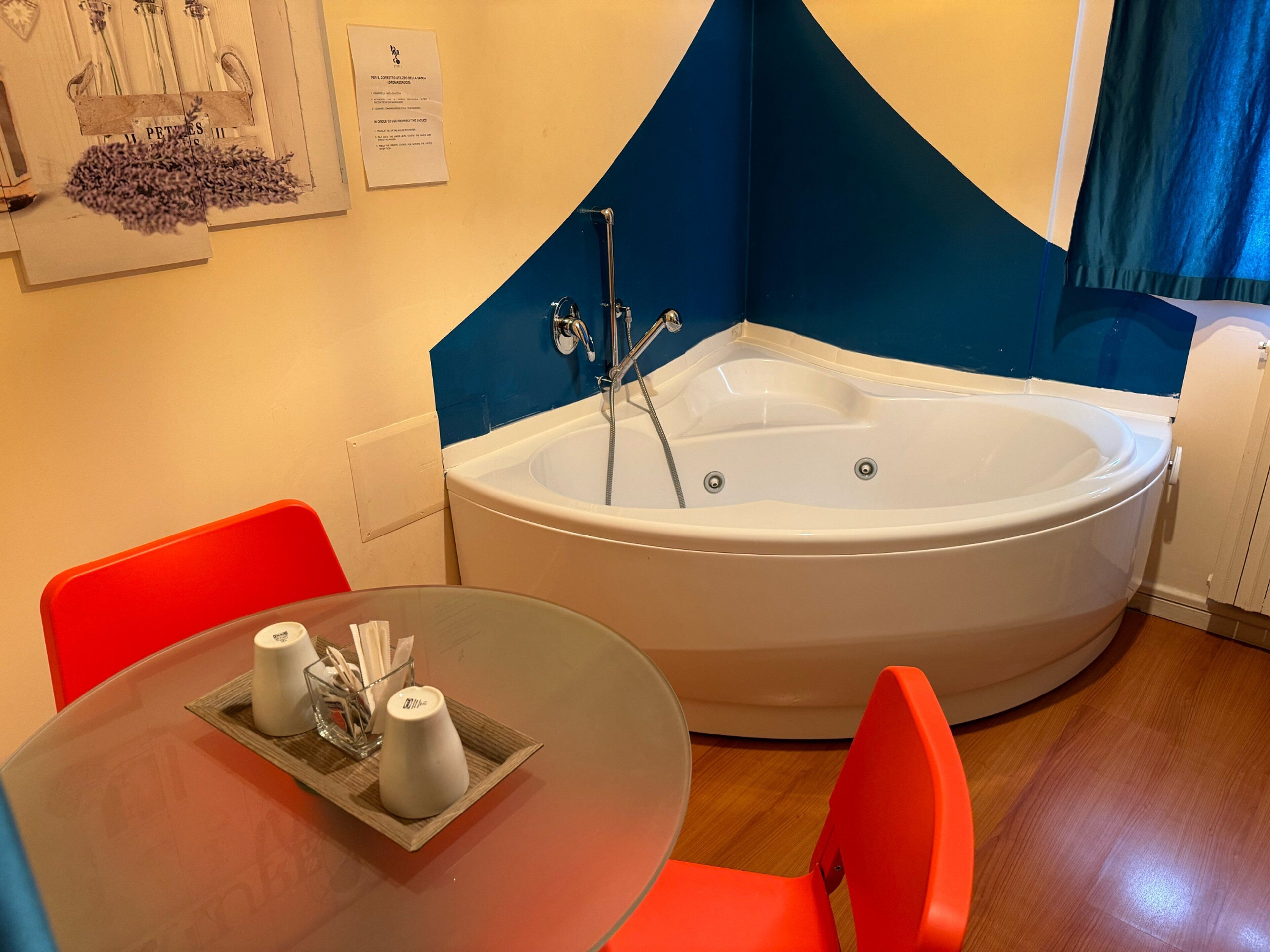 A modern bathroom with a freestanding bathtub, a round table with a tray of toiletries, and bright orange chairs.