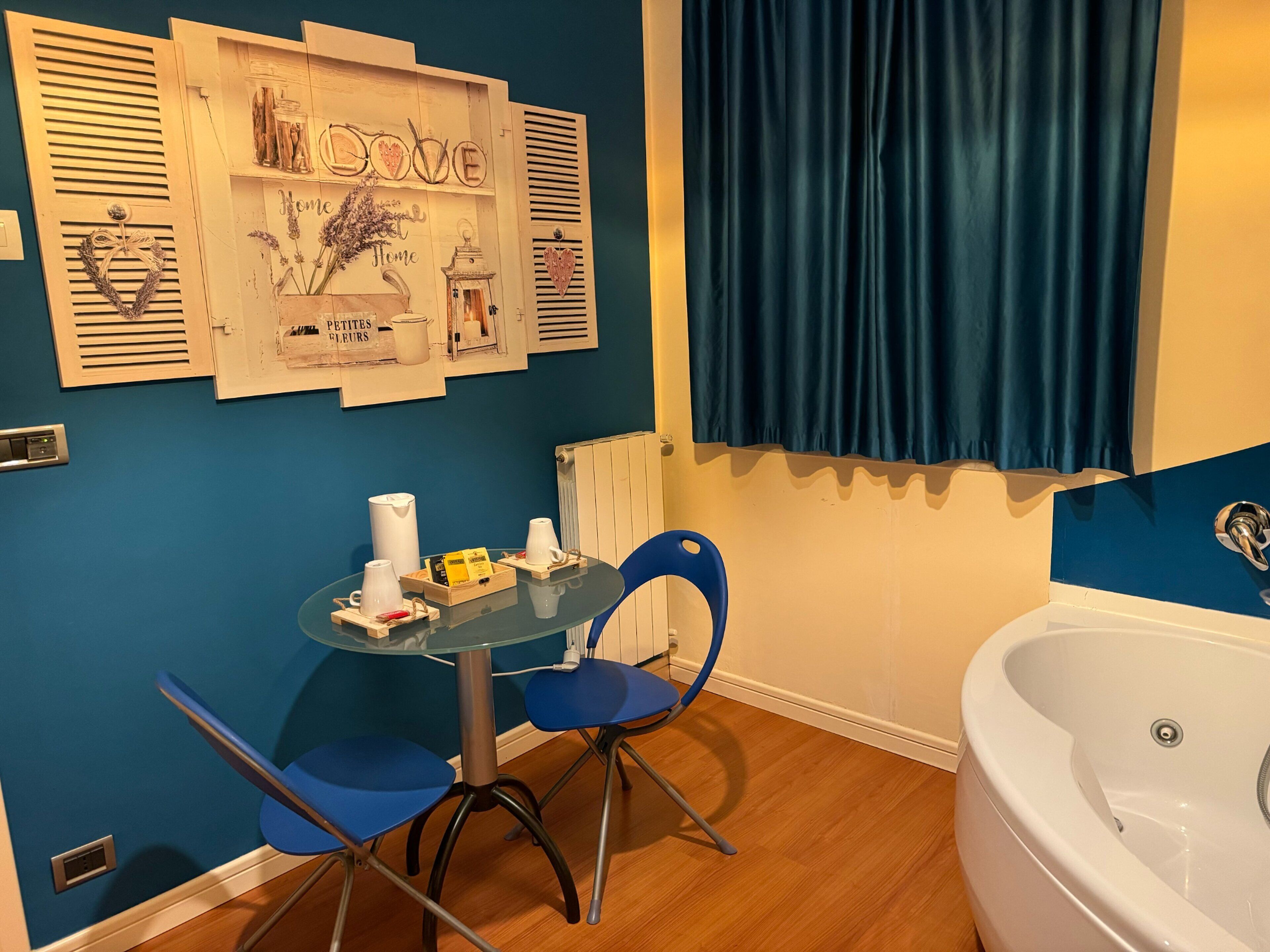 Un baño con bañera, una mesa de vidrio con sillas, una silla azul, un radiador, y una pared con adornos y un cartel que dice 