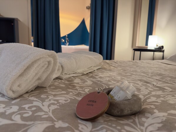 Una cama bien hecha con una toalla blanca enrollada, una mesita de noche con lámpara y una etiqueta decorativa sobre la cama.