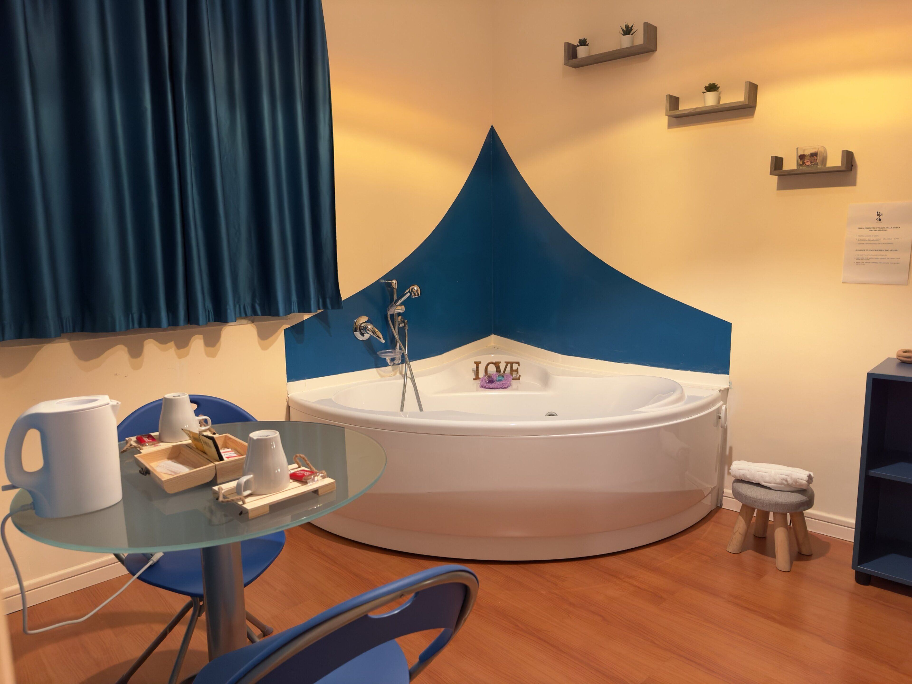 Un baño moderno con una bañera independiente, una mesita de vidrio con una tetera y tazas, y un taburete pequeño.