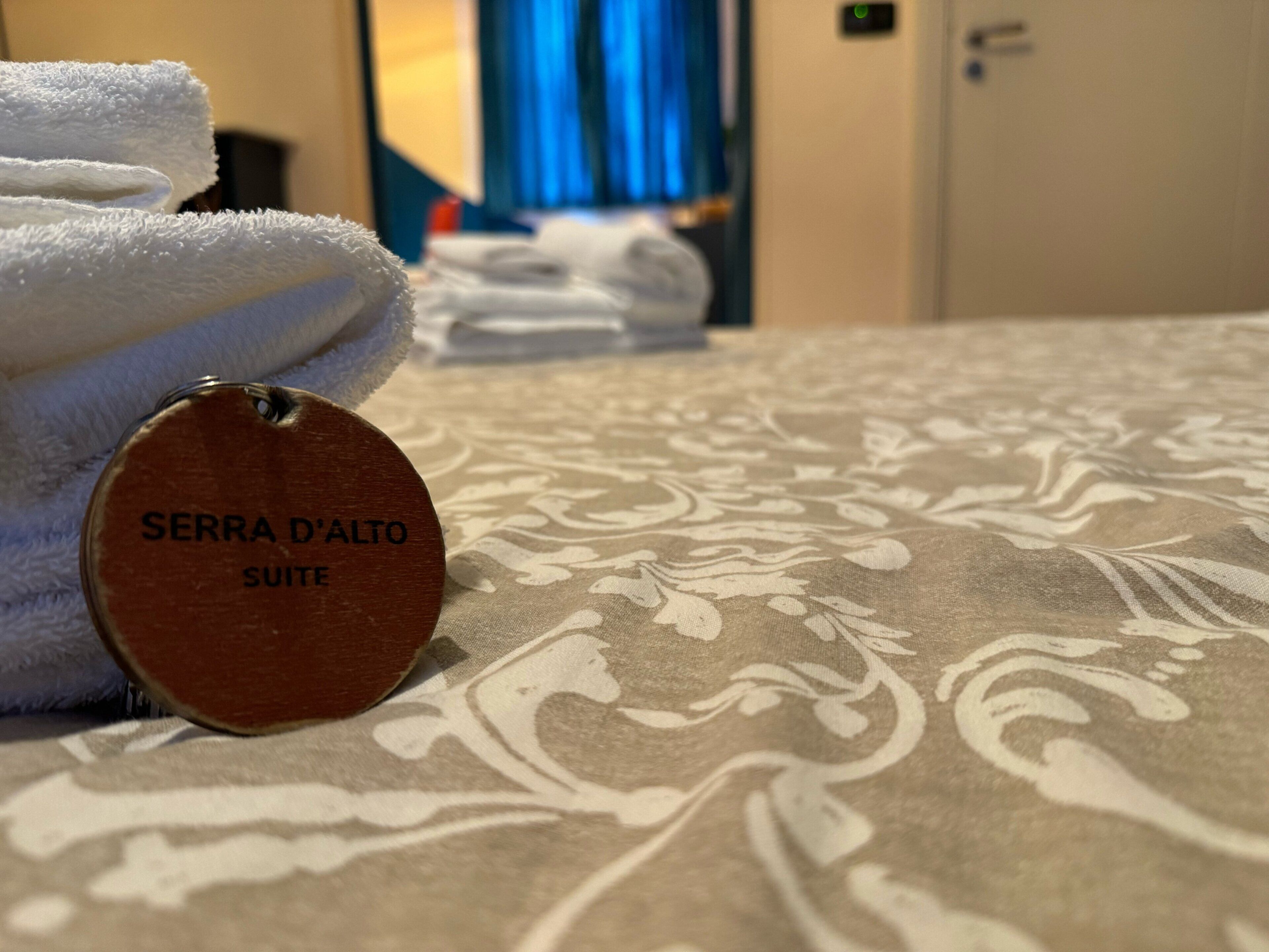 A bed with a patterned bedspread and a tag reading "SERRA D'ALTO SUITE".