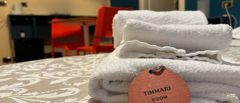 A neatly folded white towel with a tag labeled "TIMMARI ROOM" on a patterned bedspread.