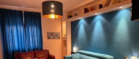 A modern living room with a blue sofa, a red leather chair, a white table, and a hanging light fixture.