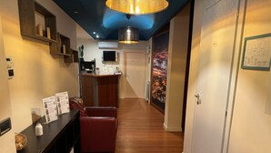 Un couloir avec un plancher en bois, un canapé en cuir rouge, un comptoir d’accueil et un luminaire au plafond.
