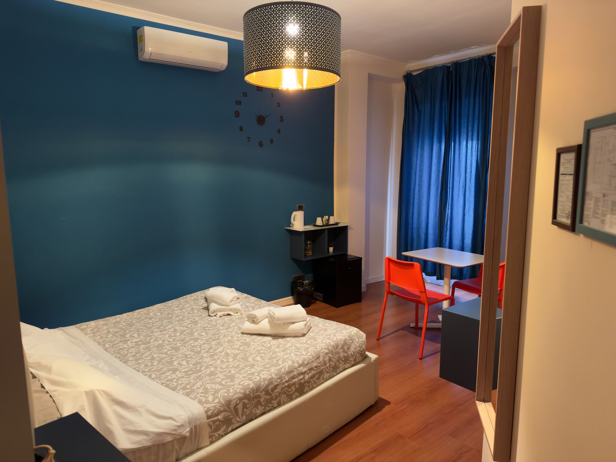 A bedroom with a bed, a desk, a chair, and a hanging lamp.
