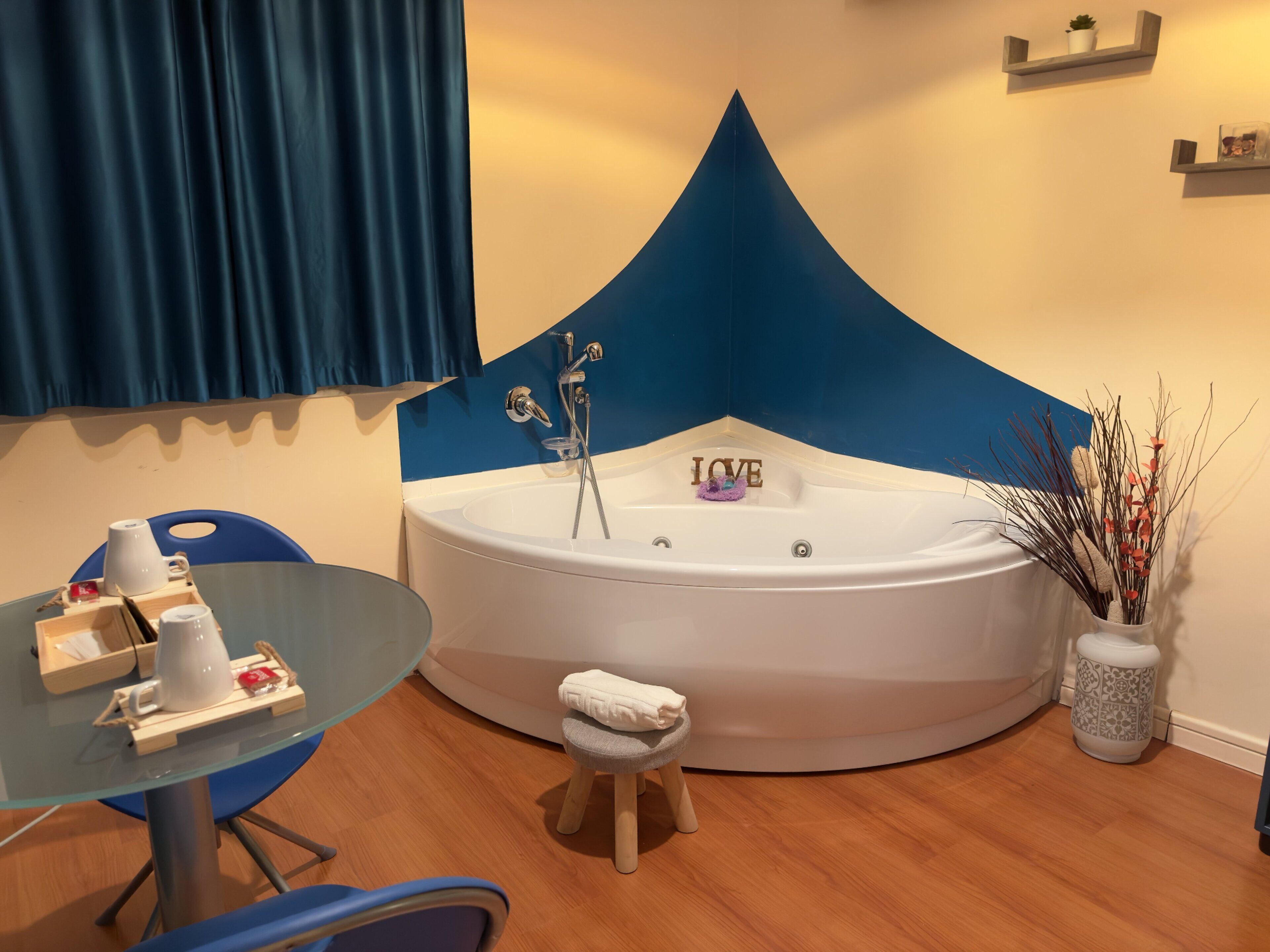 A modern bathroom with a freestanding bathtub, a glass table with toiletries, and a blue accent wall.