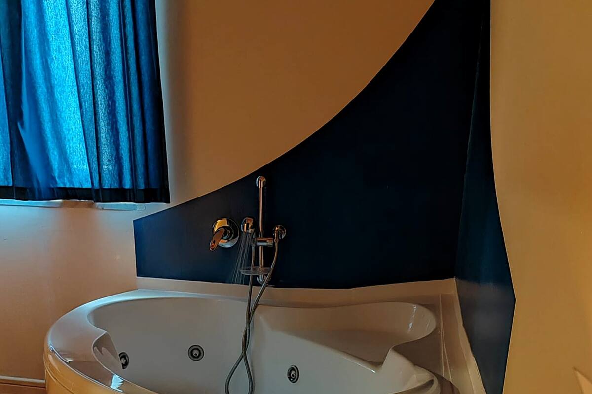 Een moderne badkamer met een vrijstaand bad, een handdouche, een brandende kaars en een klein potje badzout op een houten dienblad.