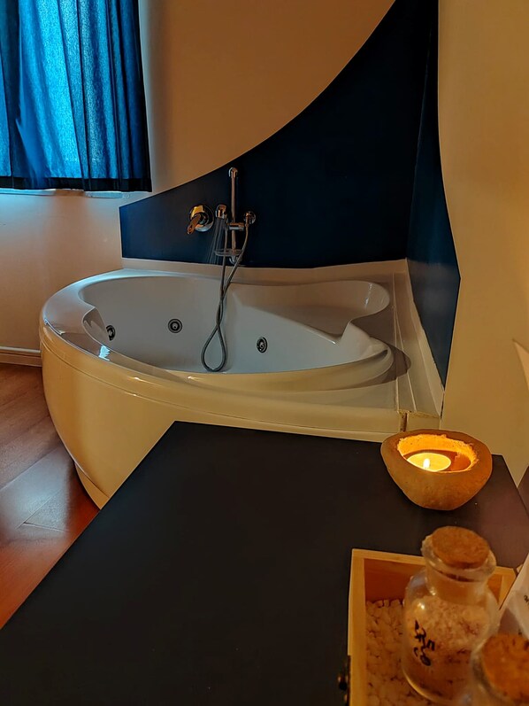 A modern bathroom with a freestanding bathtub, a handheld showerhead, a lit candle, and a small jar of bath salts on a wooden tray.