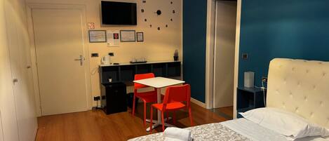 Une chambre à coucher avec un lit, un bureau et une chaise, une horloge et un téléviseur fixé au mur.