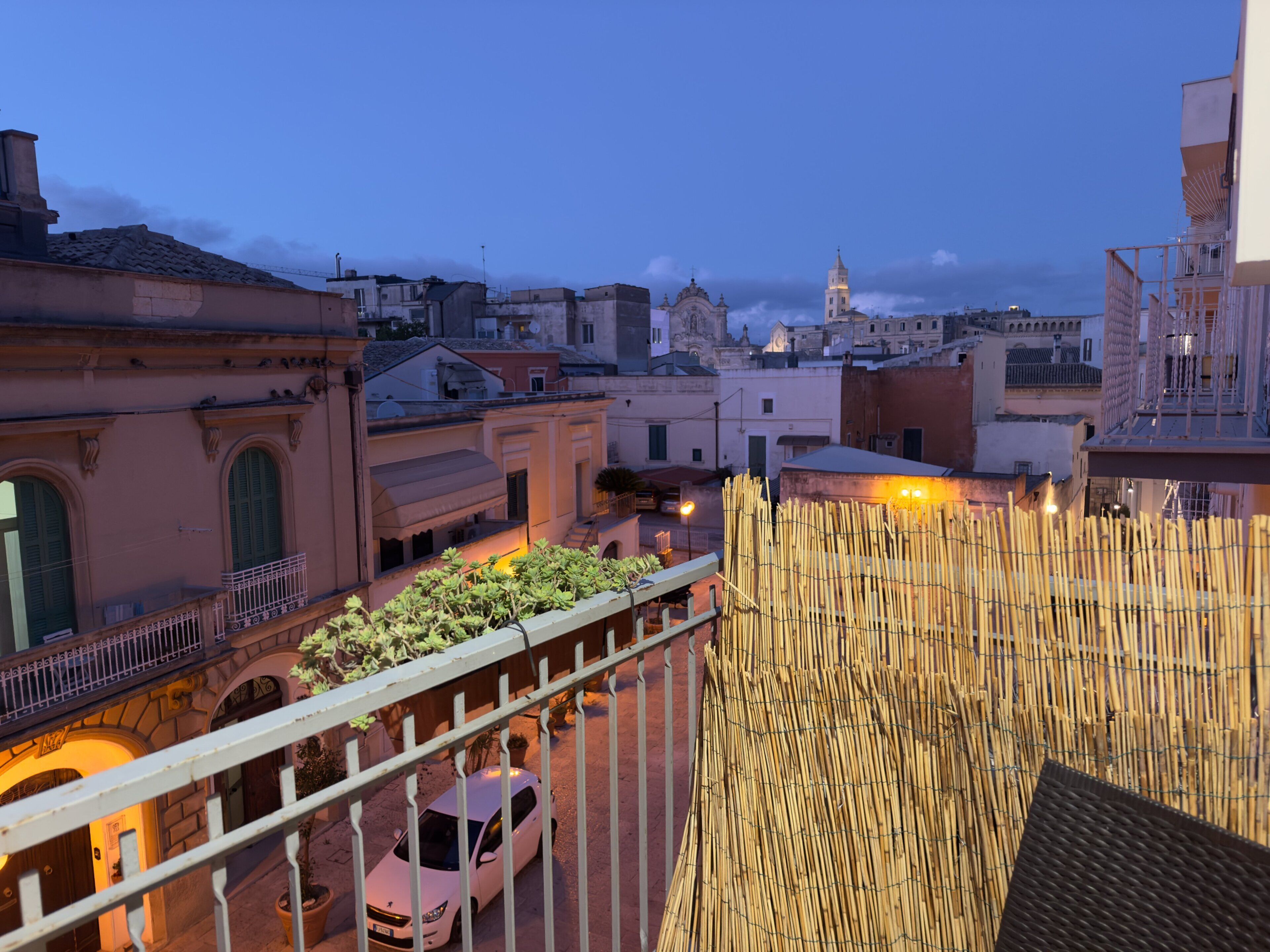 Un balcon offrant une vue sur le paysage urbain au crépuscule, avec des bâtiments et un beffroi.