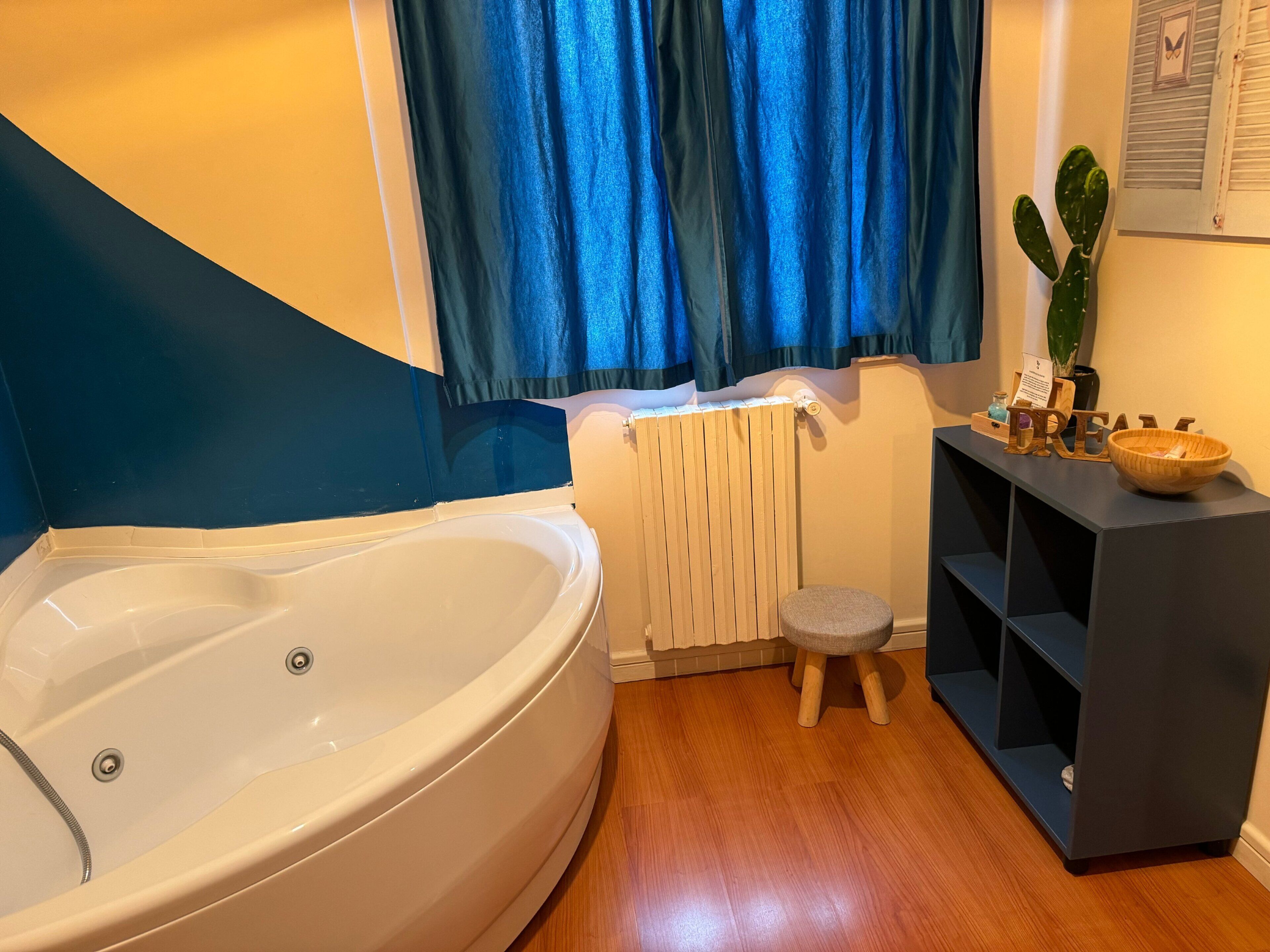 Une salle de bain avec une baignoire, un petit tabouret, une étagère avec des articles de toilette et une plante.