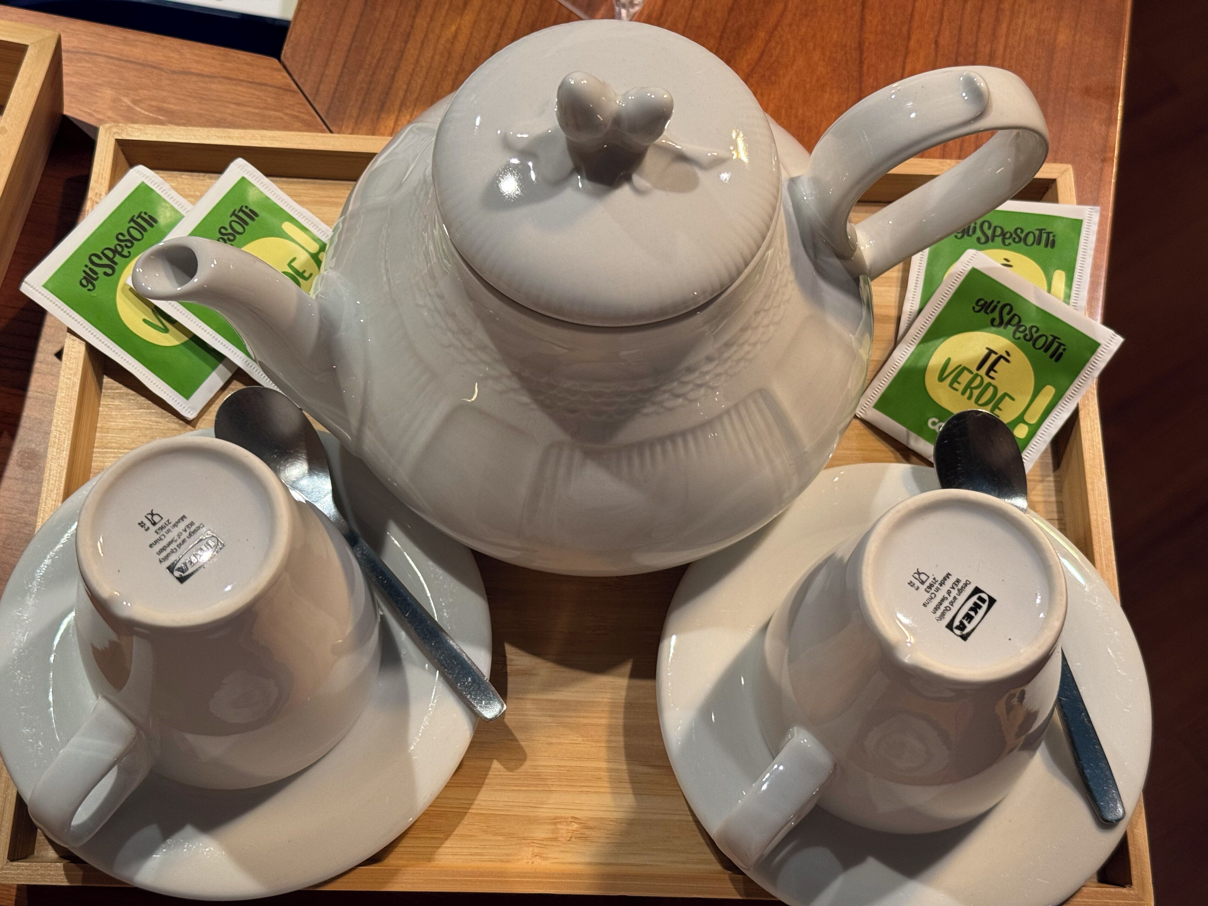 A white teapot with a lid and two matching cups on a wooden tray.
