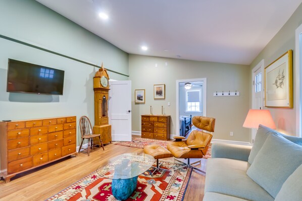 A spacious living room with a large wooden dresser, a glass coffee table, a leather armchair, and a light blue sofa.