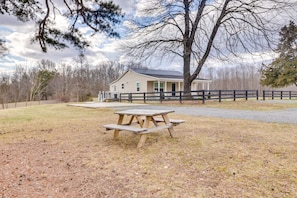 A picnic table in a grassy area with a house and a fence in the background.