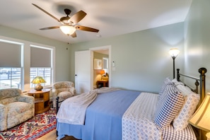 A bedroom with a bed, two armchairs, a ceiling fan, a lamp, and a window.