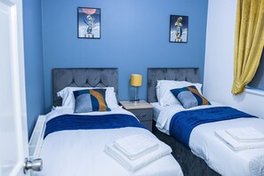 A hotel room with two beds, a nightstand, and a window with yellow curtains.