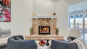 Un salon moderne avec une cheminée en pierre, des canapés gris et une grande fenêtre donnant sur un paysage.