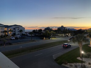 A residential street during sunset with houses, parked cars, and a clear sky.