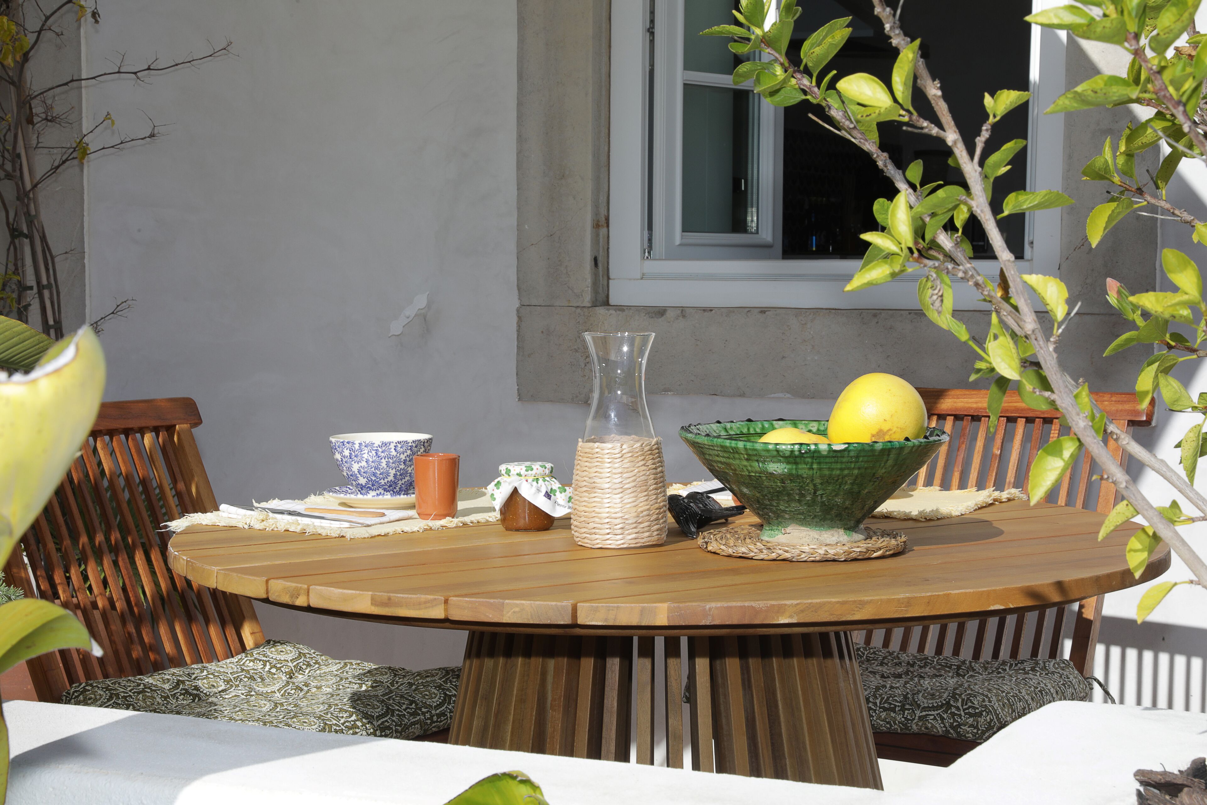 Une table ronde en bois sur laquelle se trouve un panier tressé contenant des citrons, une carafe en verre et un bol en céramique.