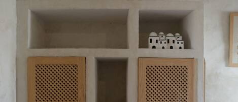 A room with two wooden louvered doors, a shelf with baskets, and a small white bed.