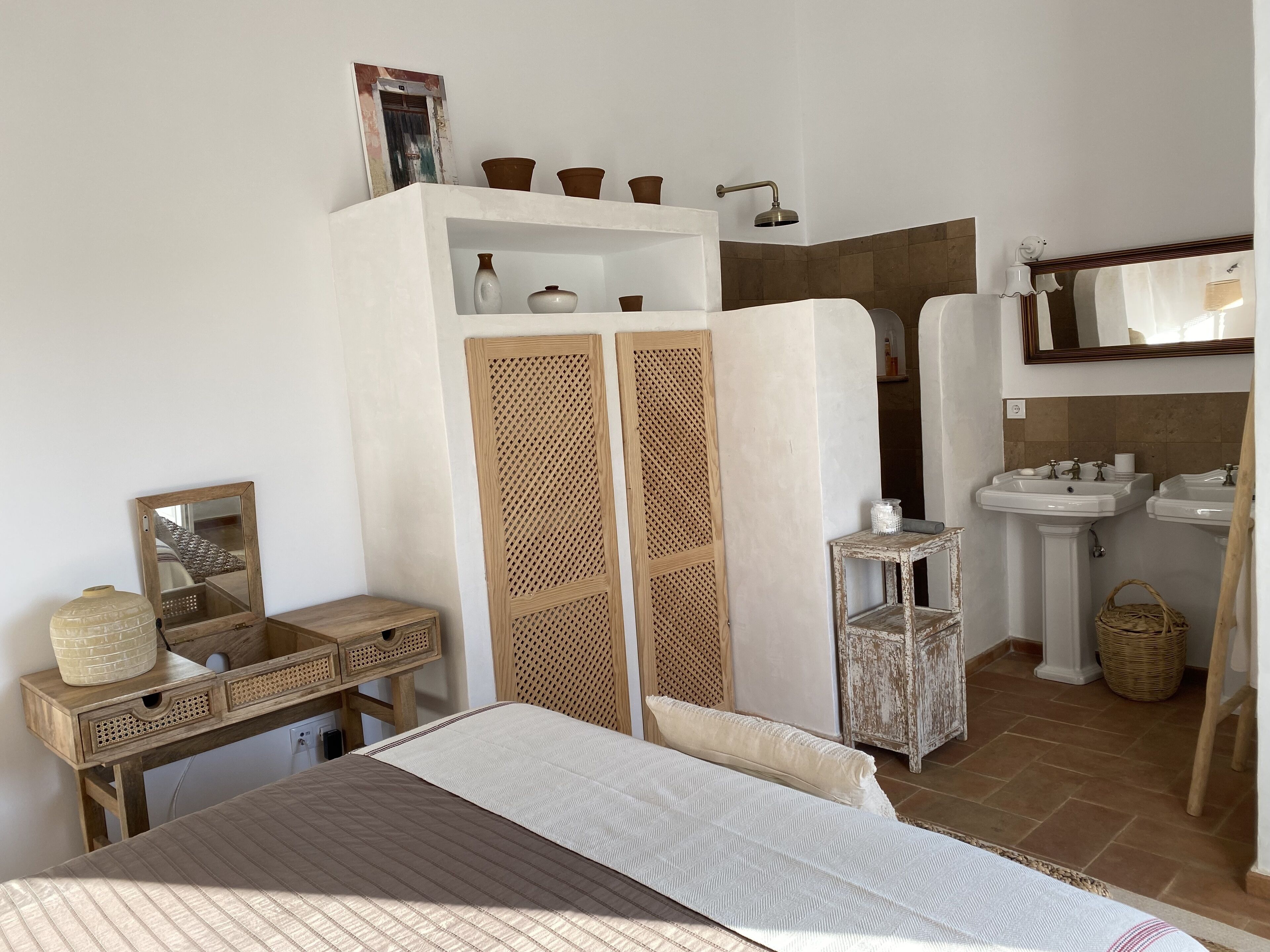 Un dormitorio con cama, mesita de noche, armario y baño con lavabo y espejo.