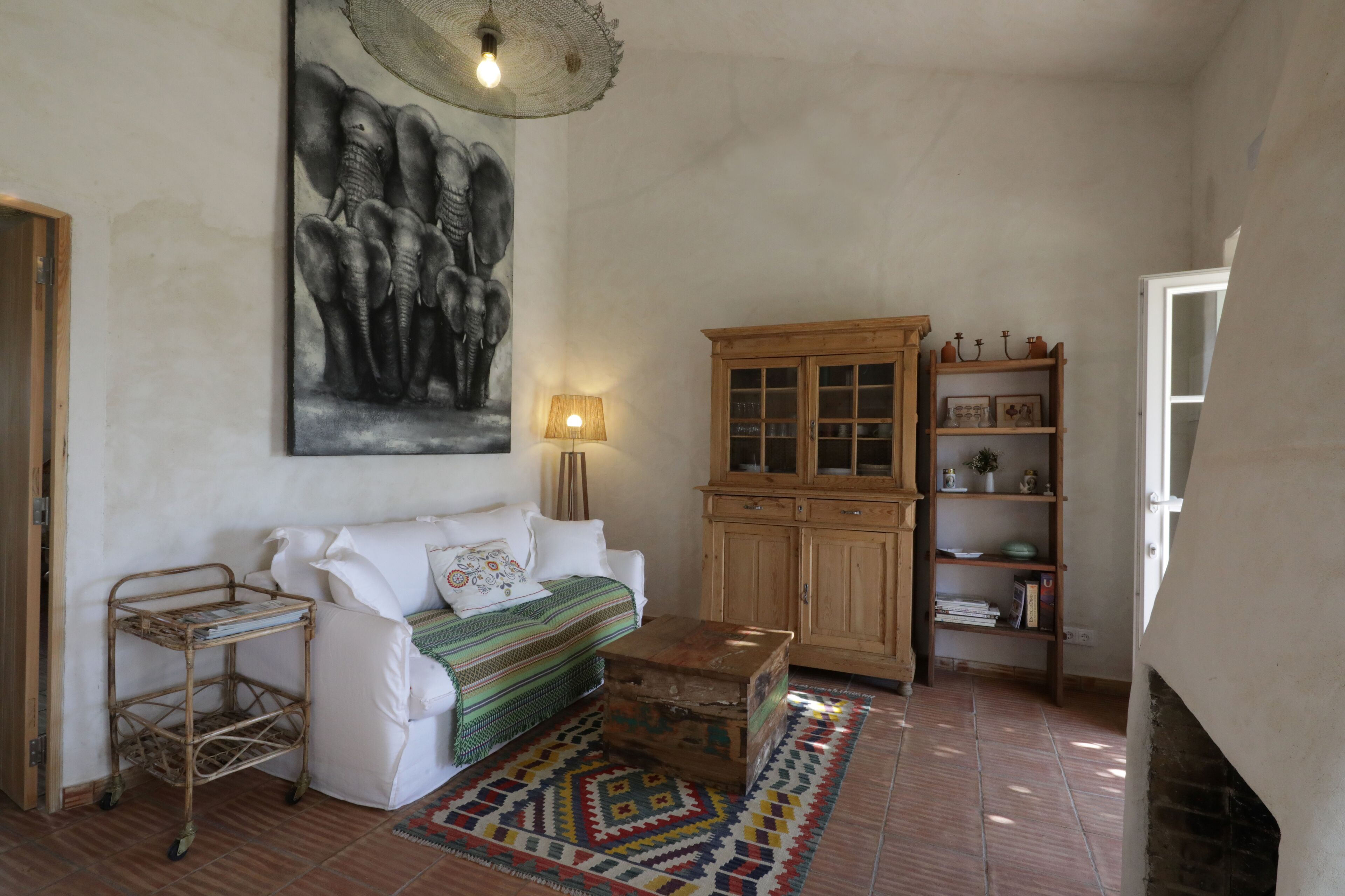 A living room with a white sofa, a wooden cabinet, a patterned rug, and a wall-mounted lamp.