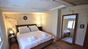 Un dormitorio con una cama de madera, una mesita de noche con lámpara, un espejo y una puerta.