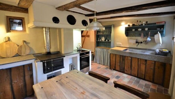 Una cocina rústica con vigas de madera a la vista, una isla central y una lámpara colgante.