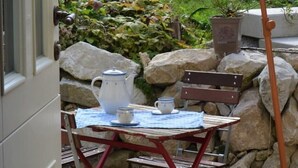 Un espacio al aire libre rústico con mesa y banco de madera, rodeado de rocas grandes y plantas en macetas.