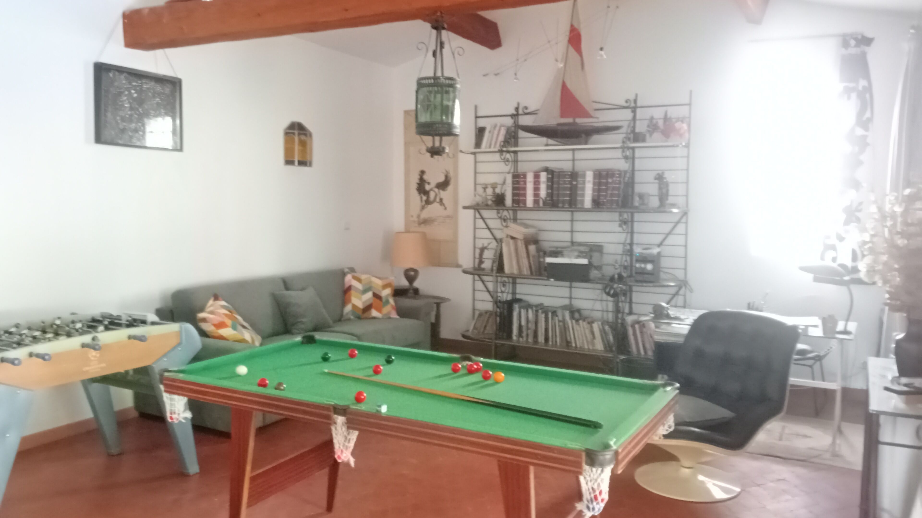 A cozy living room with a pool table, a sofa, and a bookshelf.