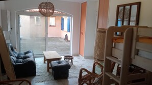 Een woonkamer met een bank, een salontafel en een rieten stoel. Er is een schuifdeur naar een buitenruimte.