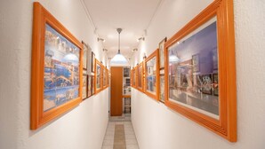 A hallway with framed pictures on the walls, a ceiling light, and a door at the end. - Room-comfort Double or Twin Room or Semi (Paros)