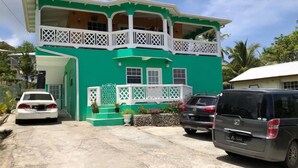A two-story building with a green facade, white balconies, and a front porch with potted plants. - Family Friendly 2-bedroom Apartment in Vieux Fort (Vieux Fort)