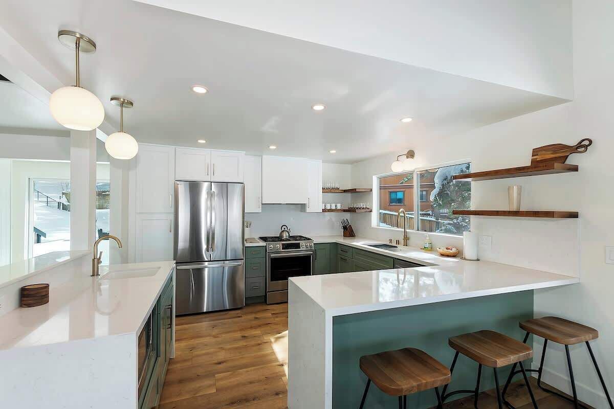 A modern kitchen with white cabinetry, stainless steel appliances, and wooden stools.