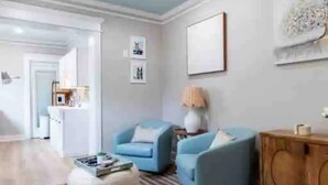 Een woonkamer met een blauwe bank, een houten kast en een kamerkleed met dessin.