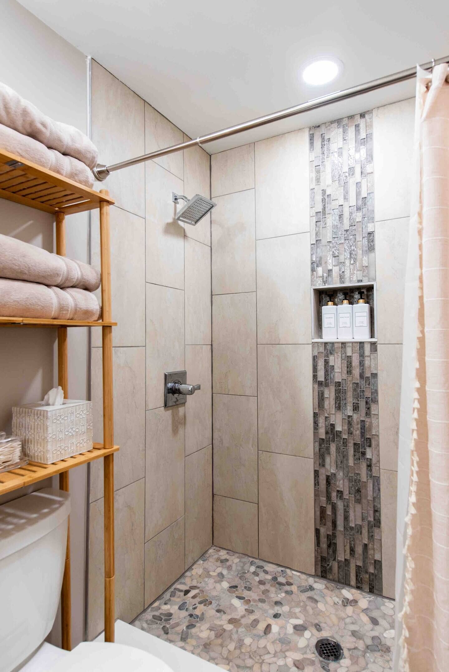 A shower area with a tiled floor, a showerhead, and a shelf with toiletries.