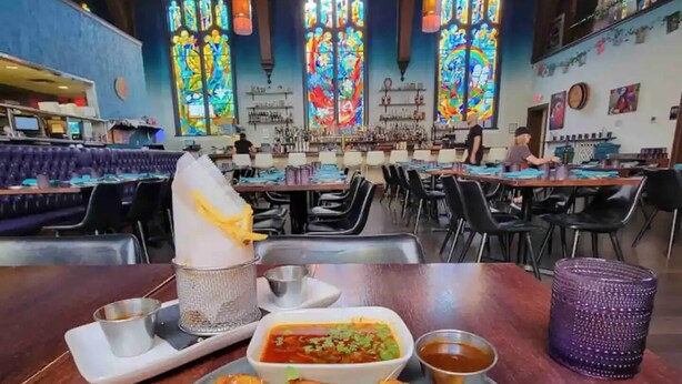Een restaurant met een bar, meerdere tafels en een groot bord quesadilla’s met bijgerechten.