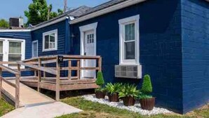 Een blauw huis met twee verdiepingen, een houten terras en bloempotten.