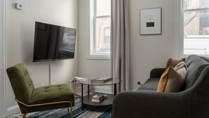 A modern living room with a flat-screen TV, a green armchair, a grey sofa, and a small round coffee table. - Flexhome East Village • Modern 2BR • Quiet Street (Chicago)