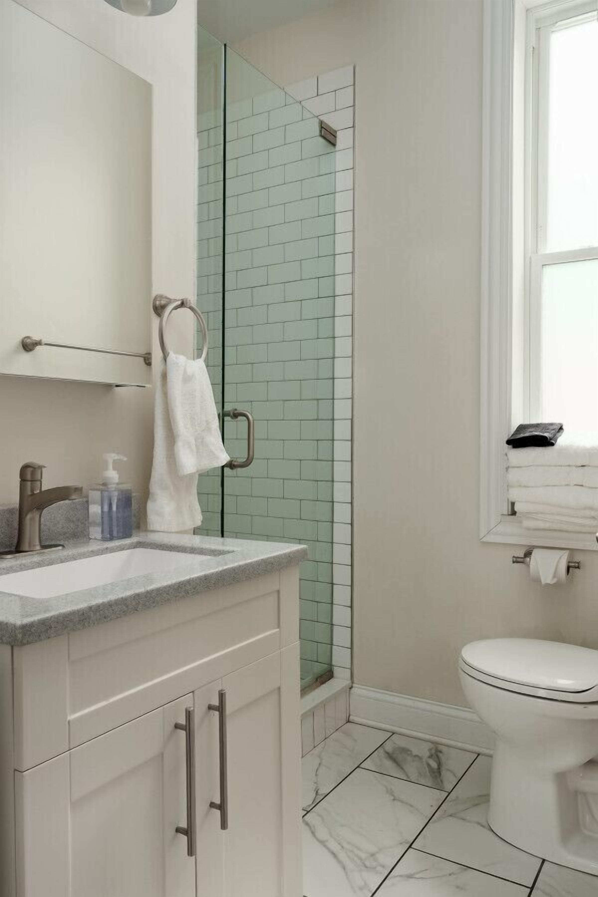 Une salle de bain avec un lavabo blanc, un miroir, un porte-serviettes, des toilettes et une douche dont les murs sont recouverts de carreaux verts.
